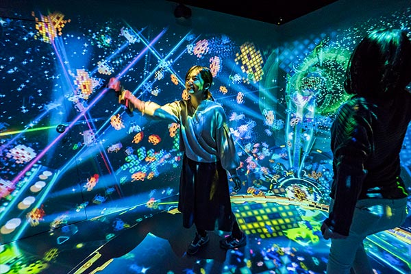 Players surrounded by colorful Space Invaders projections inside the Bahamut Disco installation